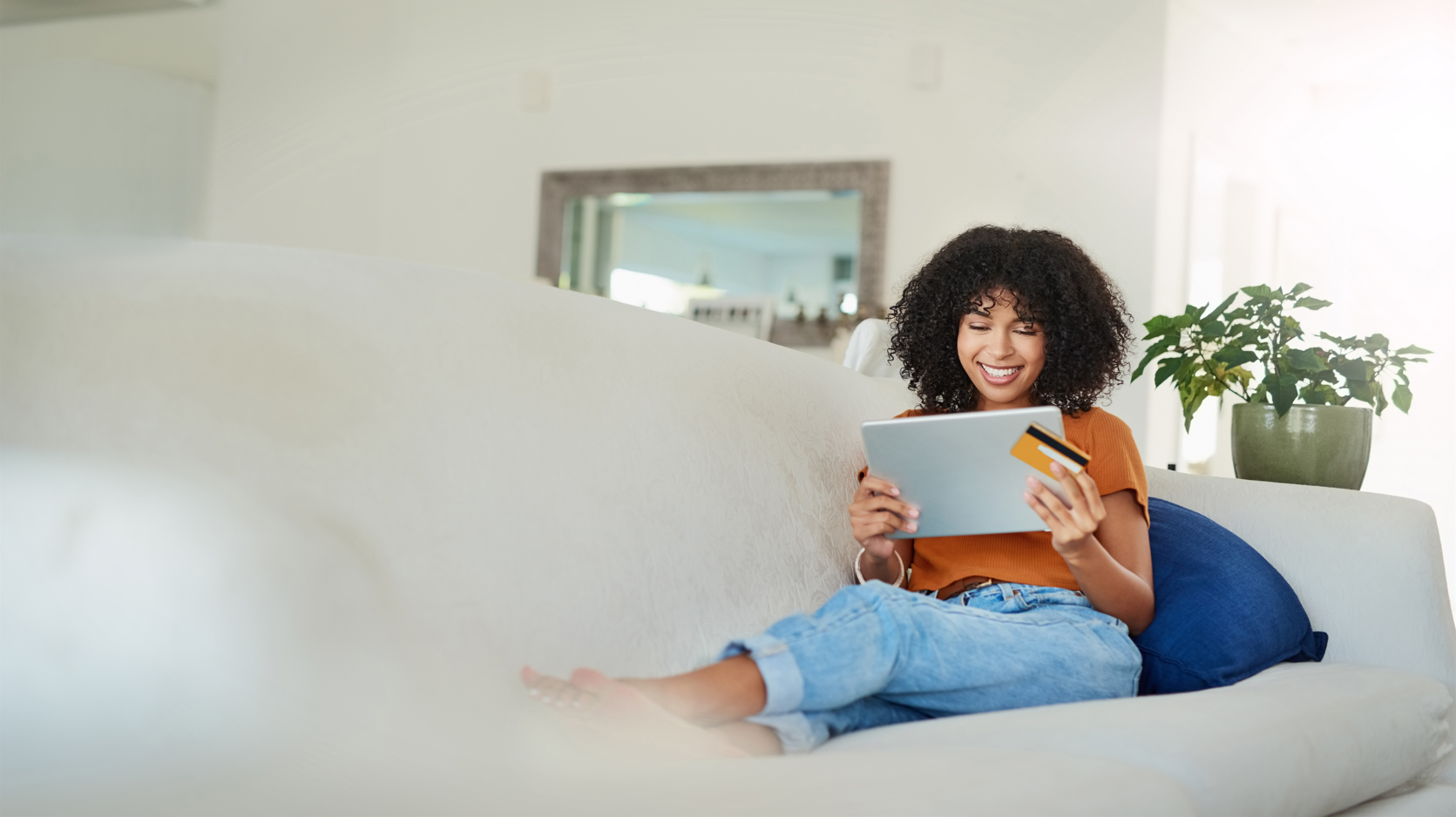 Shot of a young woman using a digital tablet and credit card while relaxing at home.